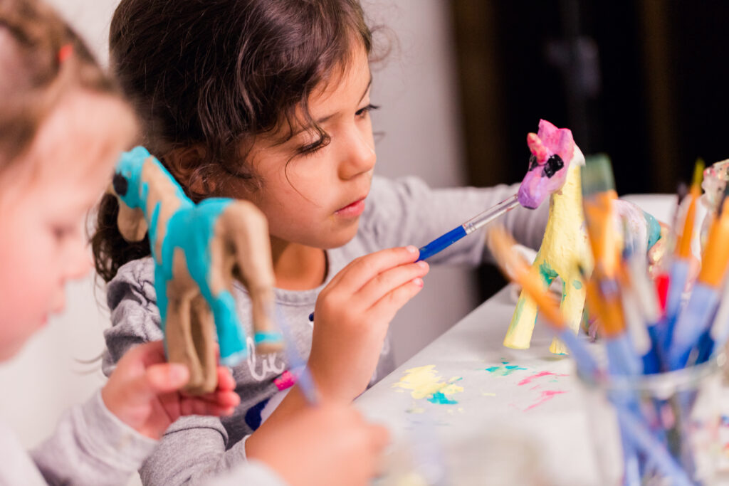 Little girls decorating small paper mache unicorn figurines.