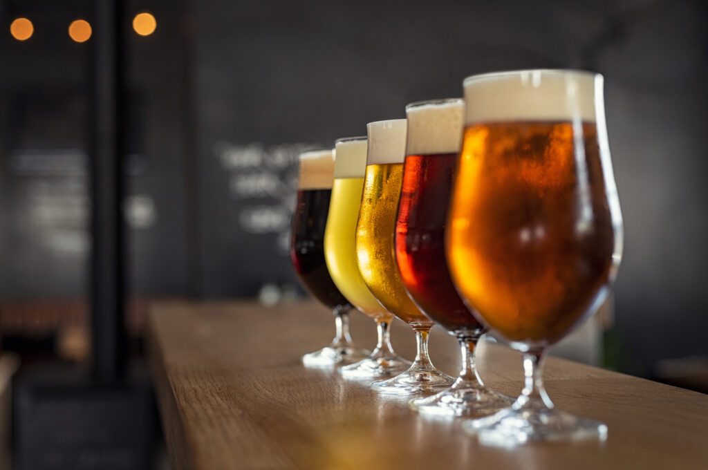 Glasses with different sorts of craft beer on wooden bar. Tap beer in pint glasses arranged in a row. Closeup of five glasses of different types of draught beer in a pub.