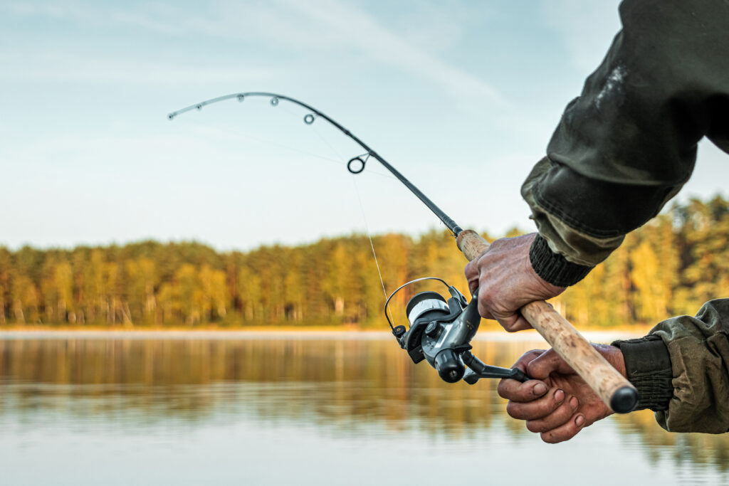 Hands of a man holding a fishing rod, a fisherman catches fish at dawn. Fishing hobby vacation concept. 