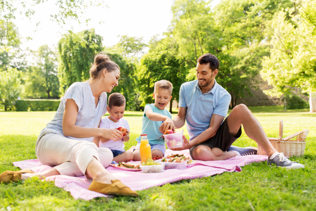 family, leisure and people concept - happy mother, father and two little sons having picnic at summer park